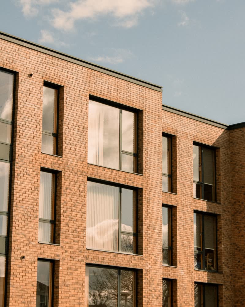 A modern tan-brick building with dark-framed windows against a pale sky.